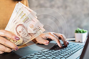 Woman hand holding banknotes and using computer laptop, make money online