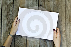 Woman hand holding blank paper on wooden table.