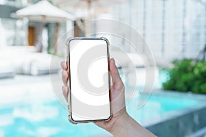 Woman hand holding blank white screen mobile phone near swimming  pool
