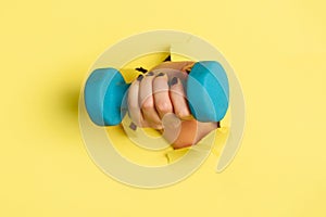 Woman hand holding blue dumbbell on yellow background. Fitness, sport, healthy lifestyle, diet concept. Banner with copy space