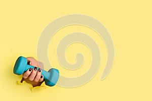 Woman hand holding blue dumbbell on yellow background. Fitness, sport, healthy lifestyle, diet concept. Banner with copy space