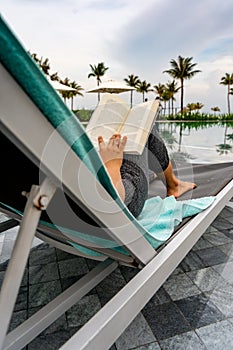 Woman hand holding book while reading at swimming pool