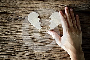 Woman hand holding broken heart paper cut on wooden background