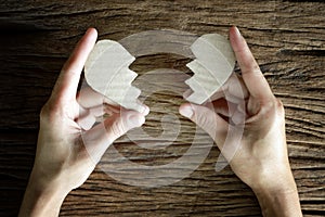 Woman hand holding broken heart paper cut on wooden background