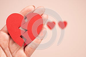 Woman hand holding broken paper red heart on pink background. Broken heart love relationship concept.