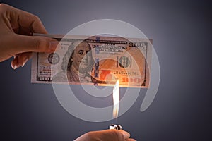 Woman hand holding burning burning dollar cash money over black background - business finances, savings and bankruptcy concept