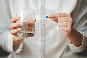 Woman hand holding capsule pill and glass of water