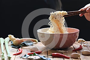 Woman hand holding chopsticks of instant noodles in cup with smoke rising and garlic on dark background, Sodium diet high risk
