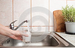 Woman hand holding a clear glass under a stream of fresh tap water from a kitchen sink faucet , soft focus close up