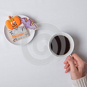 Woman hand holding coffee cup during eating funny Halloween Cookies. Happy Halloween day, Trick or Threat, Hello October, fall