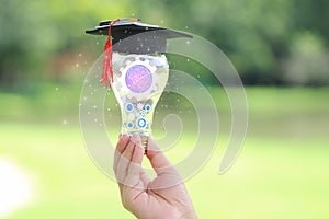 Woman hand holding cog inside in light bulb with graduates hat on natural green background, Education and Creative idea and