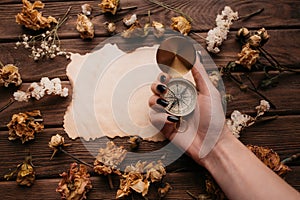 Woman hand holding compass in front of blank old paper among dry flowers.