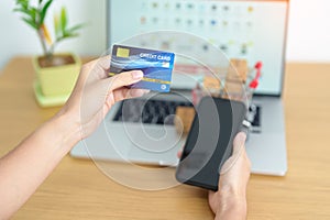 woman hand holding credit card and using laptop with mobile phone for online shopping while making order. Marketplace platform