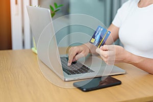 woman hand holding credit card and using laptop with mobile phone for online shopping while making order. Marketplace platform