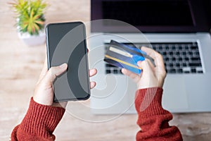 Woman hand holding credit card with using smartphone and laptop for online shopping while making orders at home. business,