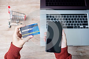 Woman hand holding credit card with using smartphone and laptop for online shopping while making orders at home. business,