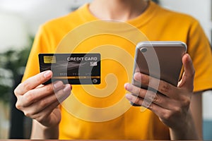 Woman hand holding credit card and using smartphone for paying products online via the Internet