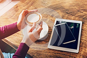Woman hand holding cup coffee in cafe with smartphone and tablet