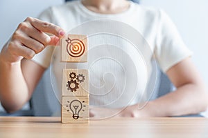 Woman hand holding dartboard above Gear and Lightbulb icon block. business planning process, goal, strategy, target, mission,