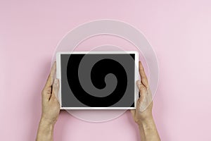 Woman hand holding digital tablet computer with blank screen mock up on pastel pink color background. Top view, copy