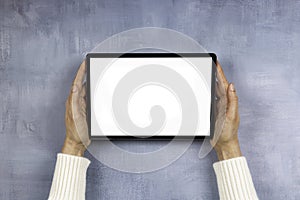 Woman hand holding digital tablet computer with blank white screen mock up on gray color background. Top view, copy