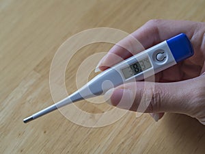 Woman hand holding electric clinical thermometer showing high fe