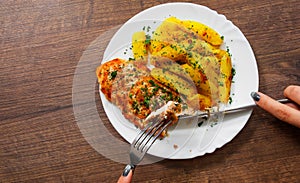 Woman hand holding fork and knife with Grilled chicken breast with potato in a plate on a wooden background