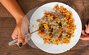 Woman hand holding fork with Rice with Vegetables and Meat in a plate on wooden table