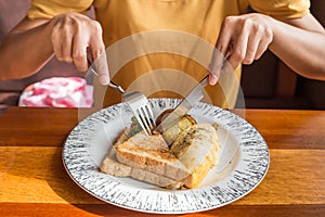 Woman hand holding fork and spoon and white plate with omelet potato, tomatoes parsley and feta cheese and bread on wooden table