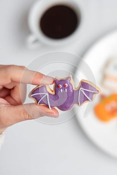 Woman hand holding funny Halloween Cookie during drinking coffee. Happy Halloween day, Trick or Threat, Hello October, fall autumn