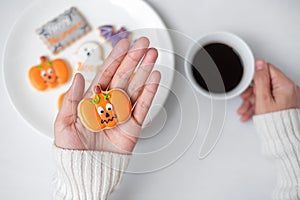 Woman hand holding funny Halloween Cookie during drinking coffee. Happy Halloween day, Trick or Threat, Hello October, fall autumn