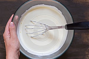 Woman hand holding glass bowl with whisked eggs and whisk in it