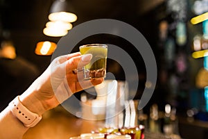 A woman hand holding a glass shot with a green alcoholic drink. Alcohol consumption