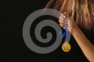 Woman hand holding gold medal against black background with glitter overlay. Award and victory concept.