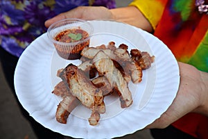 Woman hand holding Grilled pork marinated in herbs, cut into white paper plates With chili sauce
