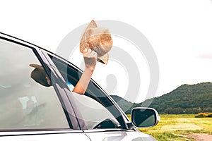 Woman hand holding hat on the car relaxing and happy traveler with mountain background