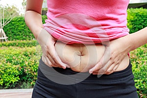 Woman hand holding her own belly fat in the park