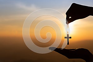 Woman hand holding holy lift of christian cross with light sunset background