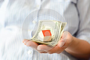 Woman hand holding house and money suggesting the rising cost of home prices