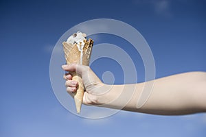 Woman hand holding ice cream cone on a hot summer blue sky background