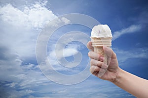 A woman hand holding Ice cream cone with summer blue sky and clouds in background,colorful picture style