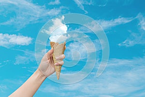 Woman hand holding Ice cream cone with white cloud with blue sky in background.