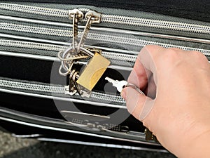 Woman hand holding the key and going to unlock the padlock on a travel suitcase zippers. Protect the baggage from theft during the