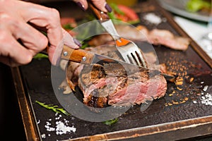 Woman hand holding knife and fork cutting grilled beef steak