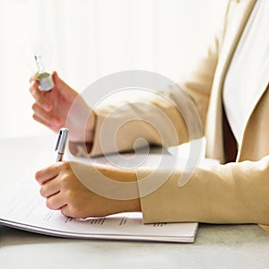 Woman hand holding light bulb, notebook, laptop, pen, documents on cream background with copy space. Creative idea, new