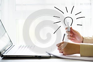 Woman hand holding light bulb, notebook, laptop, pen, documents on cream background with copy space. Creative idea, new