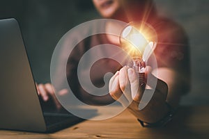 Woman hand holding light bulb and using laptop on wooden table. new idea creativity concept with innovation and inspiration.