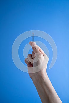 Woman hand holding match stick against blue background.