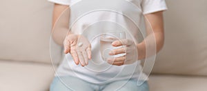 woman hand holding medicine painkiller pill and water glass on the sofa at home, taking for headaches, stomach ache, Diarrhea