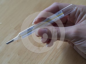 woman hand holding mercury clinical thermometer showing high fever temperature on wooden background